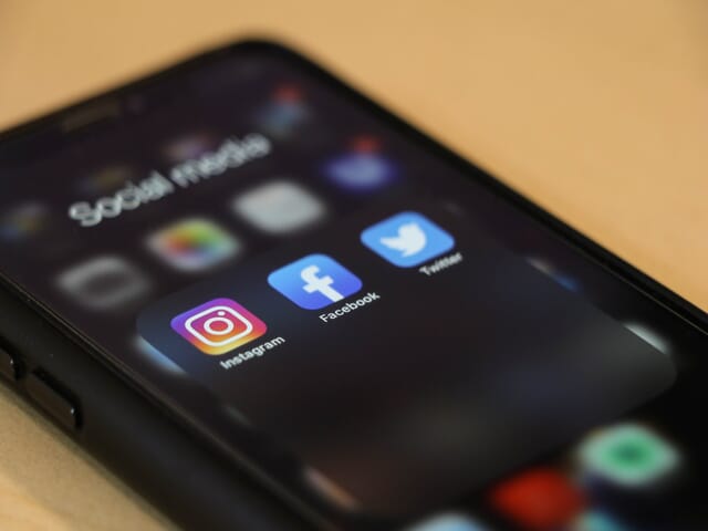 A phone laying face up showing three social media apps-Instagram, Facebook, and Twitter
